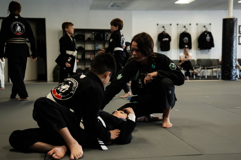 Martial arts instructor guiding children through hands-on practice of self defense moves on the mat - Self Defense