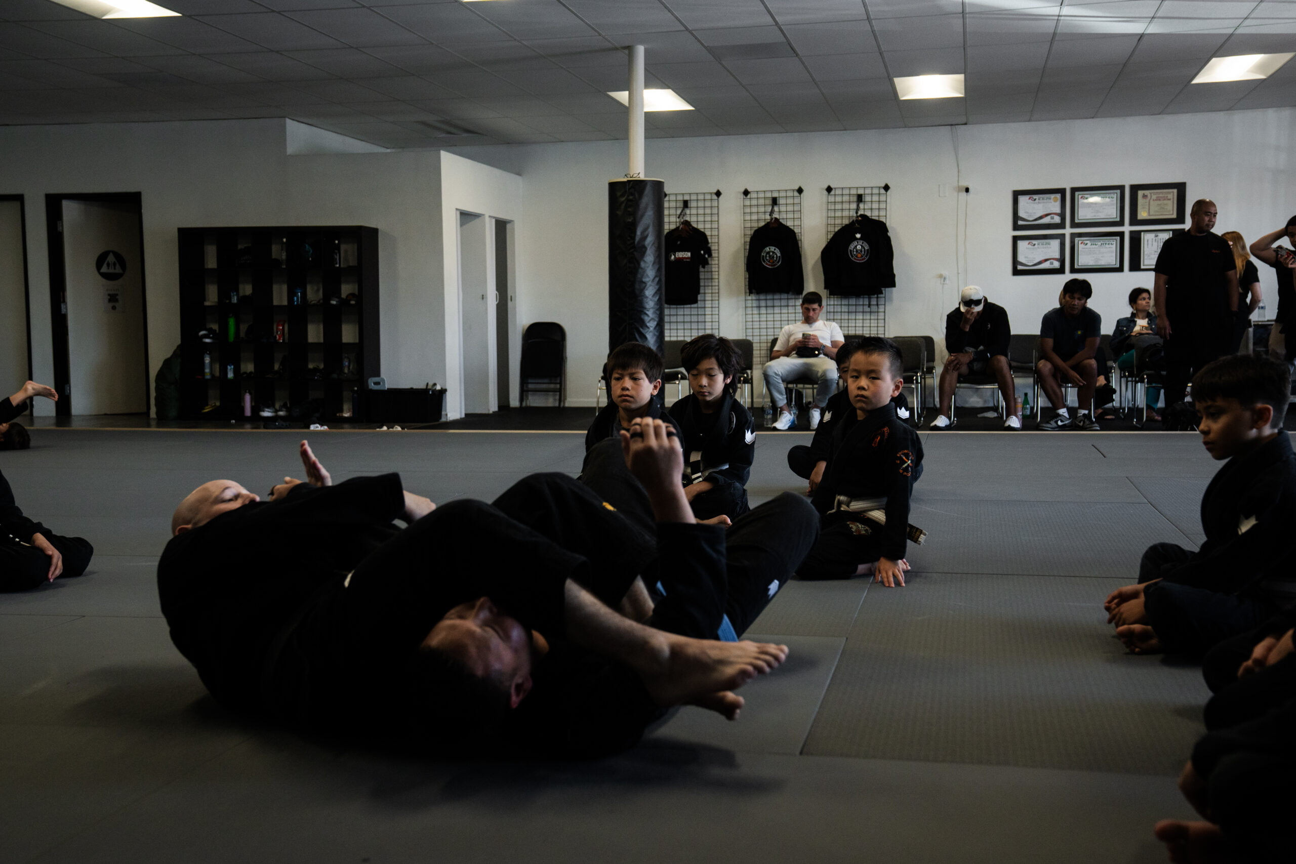 Children observing a Brazilian Jiu Jitsu instructor demonstrating a grappling technique on the mat - Brazilian Jiu Jitsu