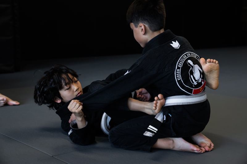 Two young students in gi uniforms sparring on the mat during martial arts kids classes - Kids Classes