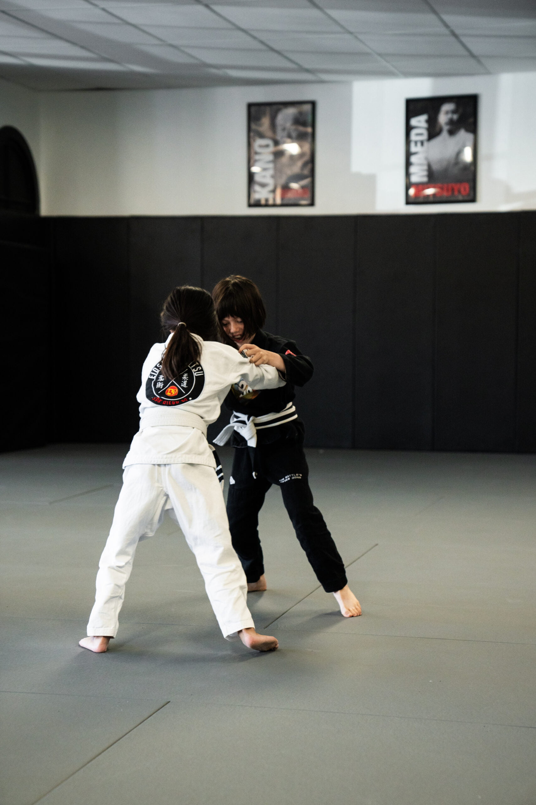 Two kids in white and black gi uniforms sparring during Judo training session on the mat - Judo