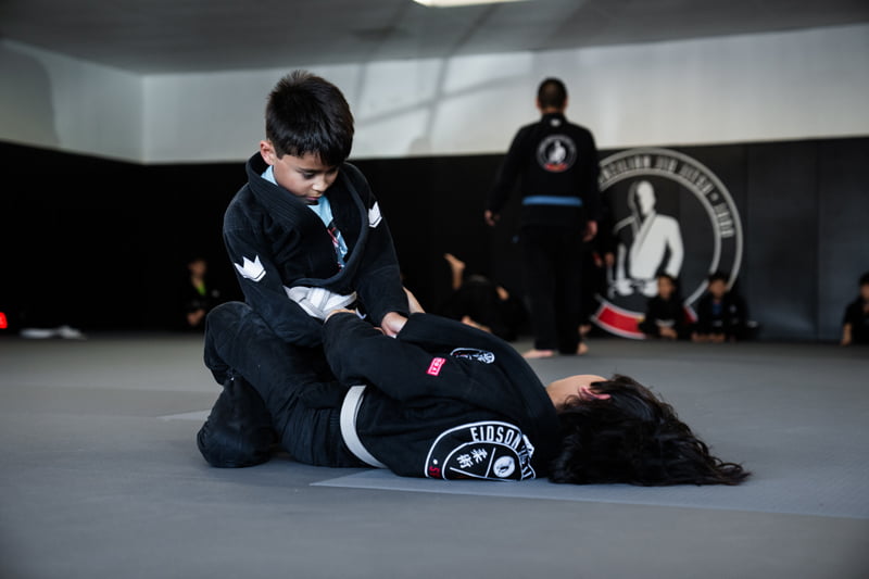 Two children in gi uniforms training on the mat, learning guard position during martial arts kids classes - Kids Classes