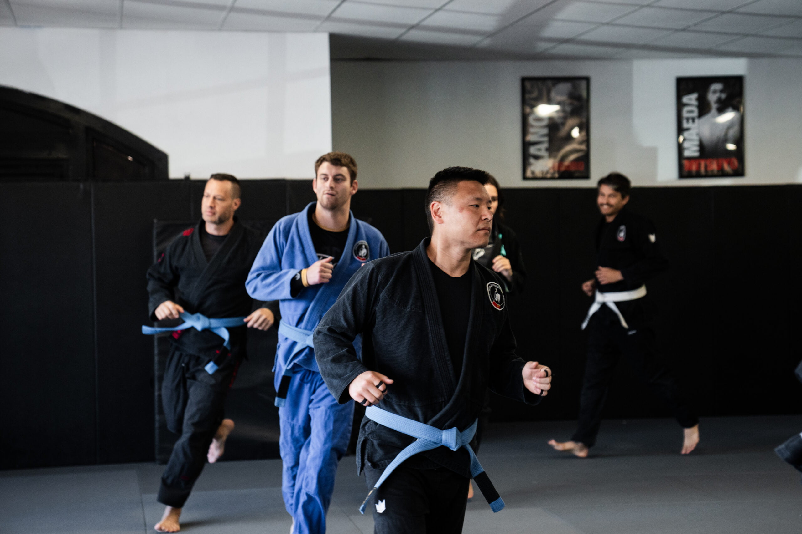 Group of adult martial arts students in gi uniforms jogging on the mat during warm-up in adults program - Adults Program