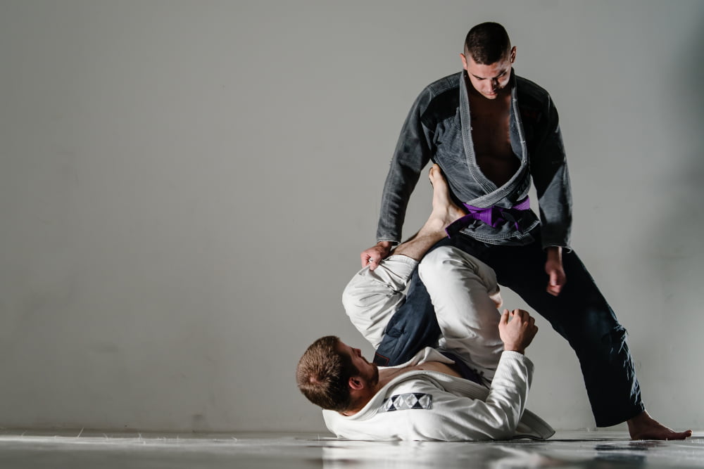 Brazilian Jiu Jitsu guard pass training - Poway Jiu Jitsu Two adult practitioners spar on the mat, one working to pass guard while the other defends using grips and hooks - Poway Jiu Jitsu