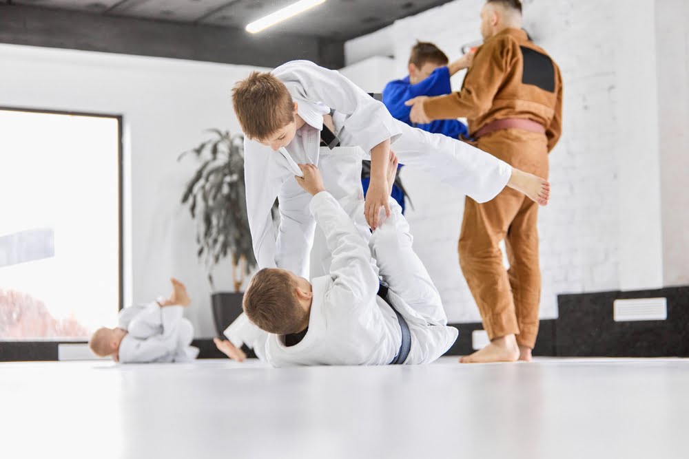 Kids practicing Brazilian Jiu Jitsu techniques - Poway Jiu Jitsu Young students in white gis learning guard and balance drills during a children’s Jiu Jitsu class - Poway Jiu Jitsu